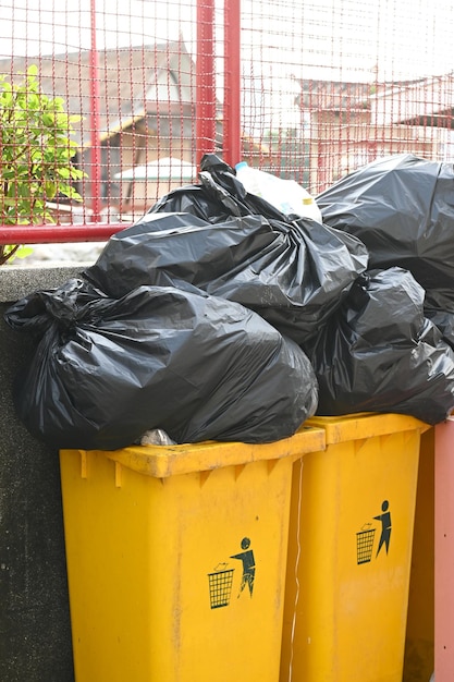 Pile of black plastic bags that contains garbage in the public yellow bins . Waiting for the rubbish