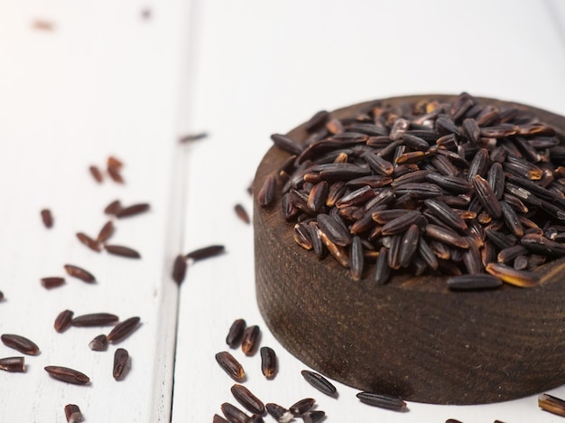 Pile of black rice in a wooden bowl on a wooden table closeup