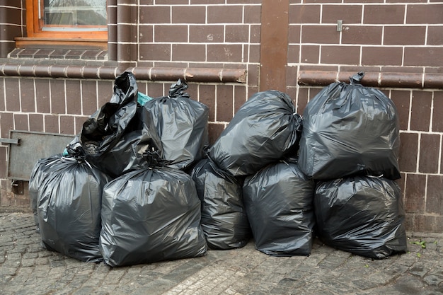 Il mucchio delle borse di rifiuti nere ha riempito di immondizia vicino al muro di mattoni sulla via