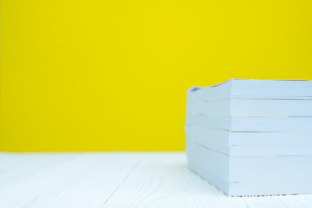 Pile of book on white table with yellow background.