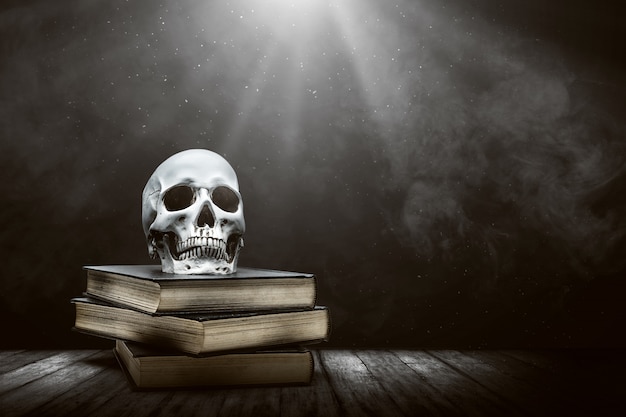 Pile of the book with a human skull on a wooden table