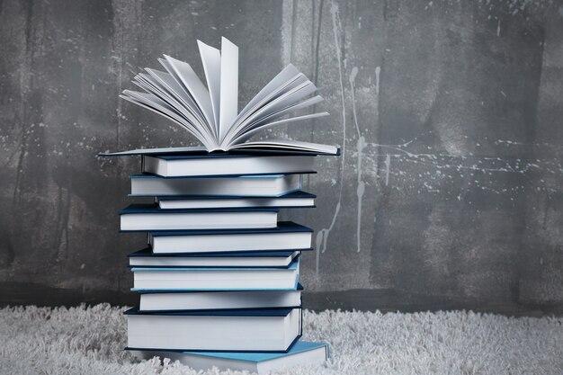 Pile of books on carpet against gray wall