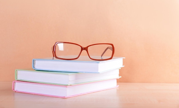 Pile of books and eyeglasses on it against beige background