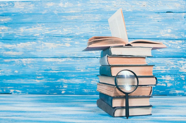 A pile of books and a magnifying glass on a blue background