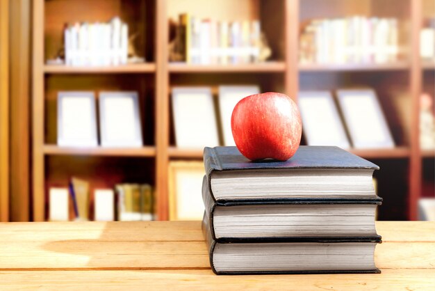 Pile of books with apple on the wooden table in library