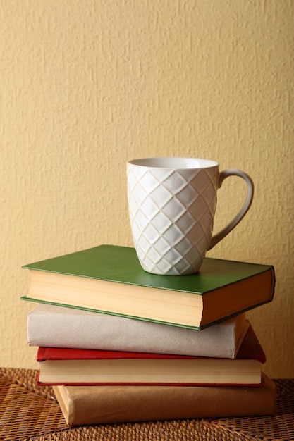 Pile of books with cup on wicker surface and light wall background