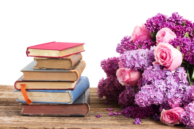 Pile of books with lilac and rose flowers isolated on white