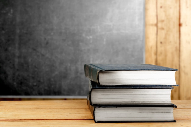 Pile of books on wooden table with blackboard