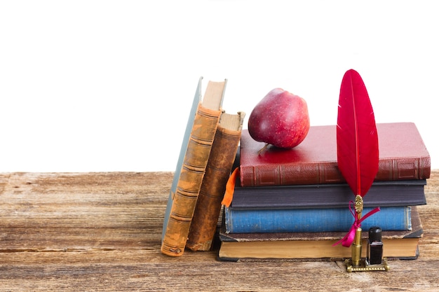 Pile of books on wooden table with feather pen isolated on white