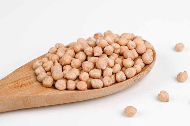 Pile of chickpeas on a wooden spoon and scattered on the white surface