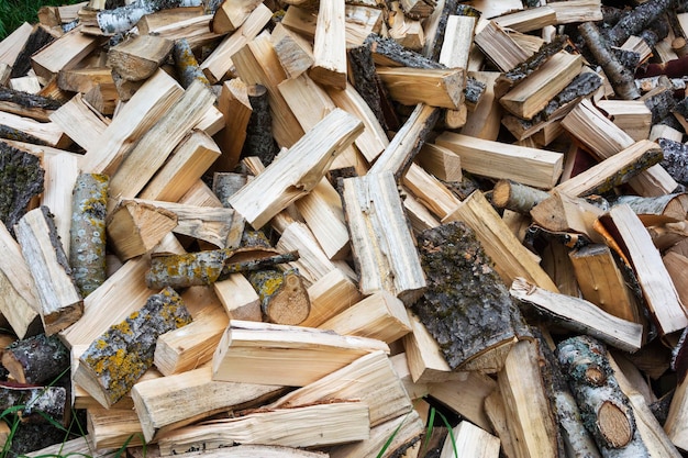 A pile of chopped birch wood is poured out on the grass in front of the fence stove heating fuel