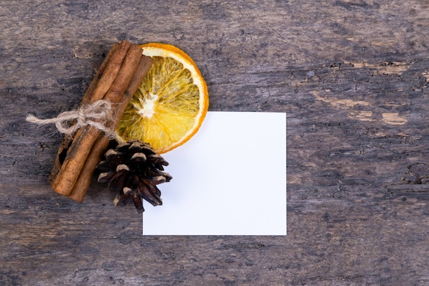 A pile of cinnamon sticks, dried orange, tree cone and white empy piece of paper with copy space.  or letter