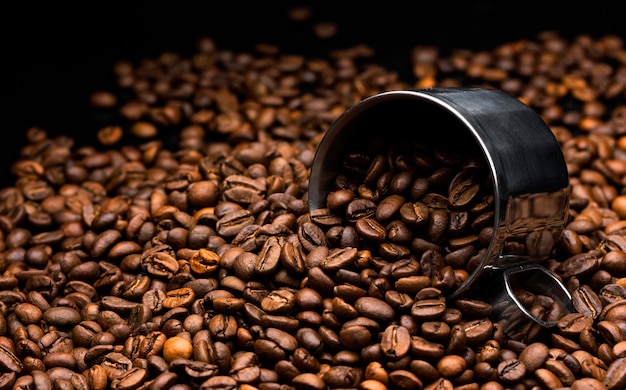 Pile of coffee beans with metal cup, close up, dark background 