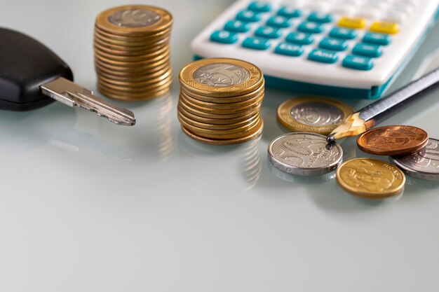 Pile of coins, calculator and pencil on white table