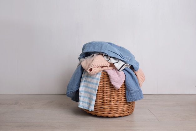 A pile of colorful clothes falls out of a wicker Laundry basket on a light background