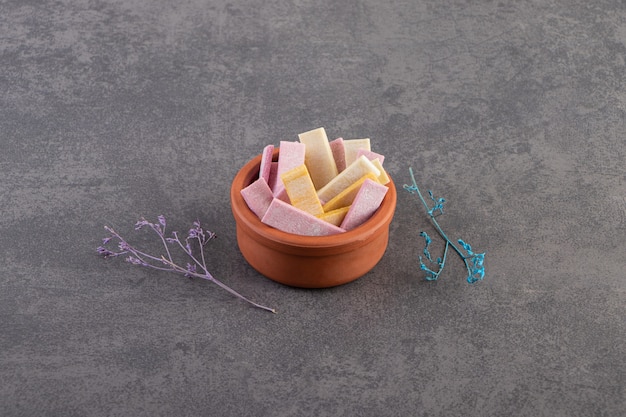 Pile of colorful gums in pottery bowl over grey background. 