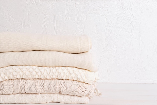 Pile of cozy white knitted clothes for cold weather Comfort organic sweaters Hygge style idea