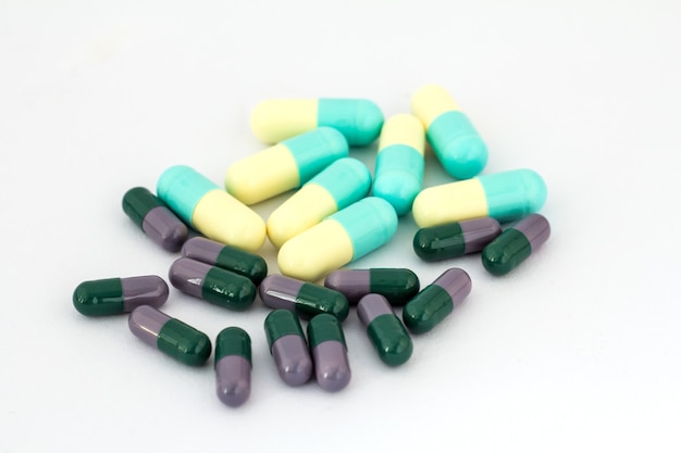 Photo pile of deifferent pills on white backgroundg. dark green and lilac, light yellow and blue cupcules