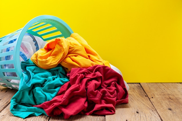 Pile of dirty laundry in washing basket on wooden plank yellow background.