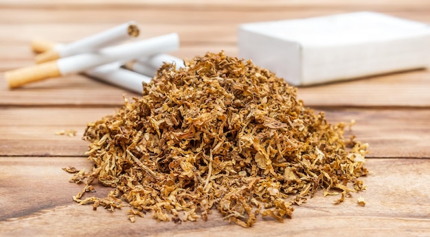 Pile of dry cut tobacco with cigarettes and pack of cigarettes on wooden table