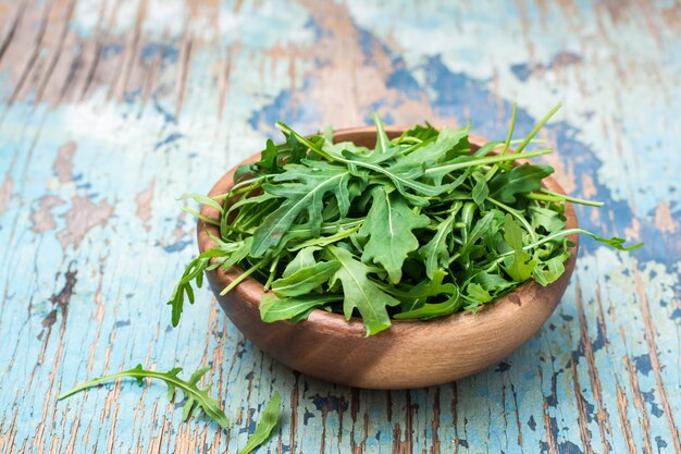 A pile of fresh arugula leaves in a wooden bowl on a wooden table