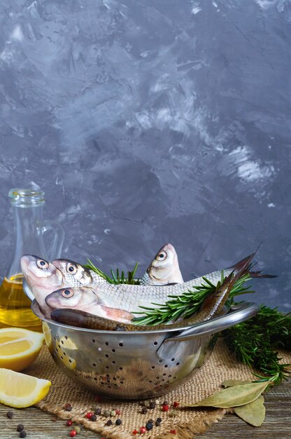 A pile of fresh raw fish with spices, lemon, rosemary on a wooden background. Fresh catch. Vertical view