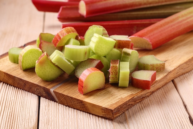 Pile of freshly cut pieces of sour rhubarb on a wooden board on table. Cultivated plant, which eaten as a fruit after cooking.