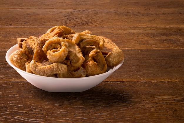 Pile of fried bacon cube portion in a white plate on wooden table.