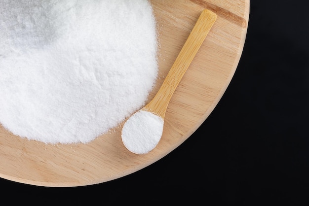 Photo pile of glucose or grape sugar in a spoon on a wooden board black background