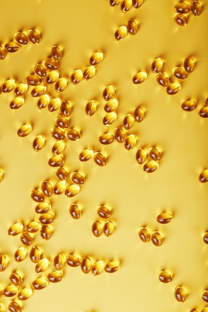 Pile of golden capsules of vitamin D3 on a yellow background with free space