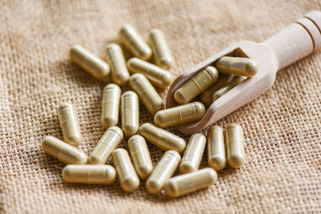 Photo pile of herbal capsules on wooden scoop from herbs on sack