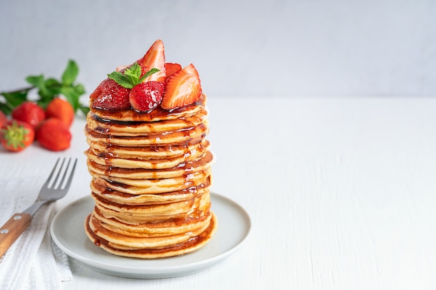 pile of homemade pancakes decorated with strawberries mint leaves and syrup topping on plate