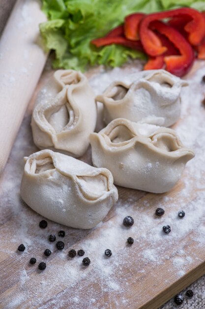 Pile of homemade raw khinkali dumplings closeup with vegetables on the board