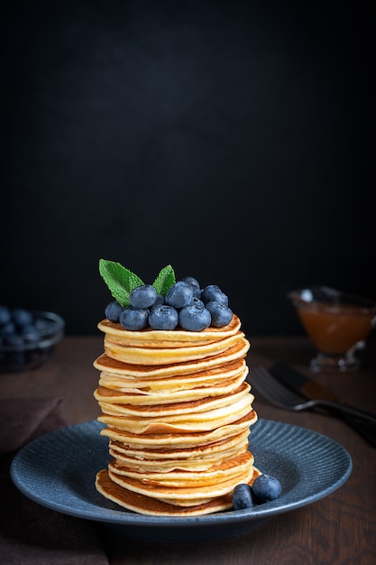 pile of homemade sweet pancakes stack with ripe fresh blueberries and  green mint leaves topping