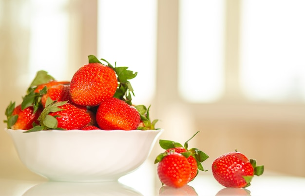 Pile of juicy red strawberries in a ceramic plate at the kitchen. Space for text