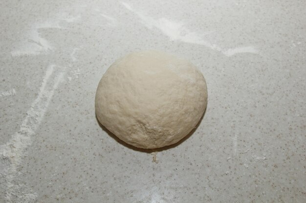 A pile of kneaded dough sprinkled with wheat flour is lying on a white kitchen table Top view baking cooking