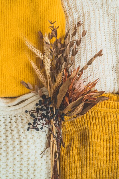 Pila di vestiti a maglia colore con bouquet di fiori secchi