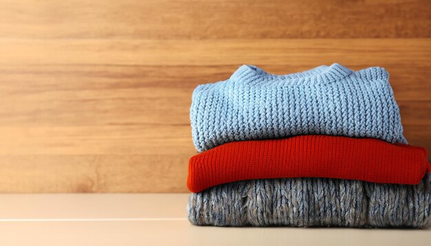 Pile of knitted winter clothes on wooden background sweaters knitwear space for text