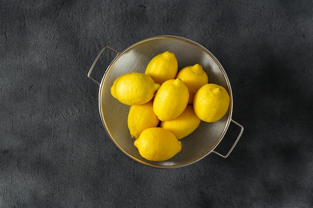 Pile of lemons in colander on a dark  top view