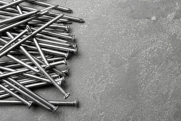 Pile of metal nails on grey stone background flat lay Space for text