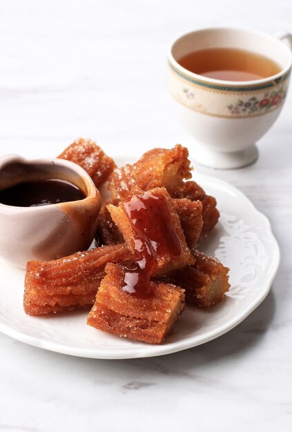 A Pile of Mini Churros or Churro with Chocolate Sauce Jam, Served with Tea. Close Up