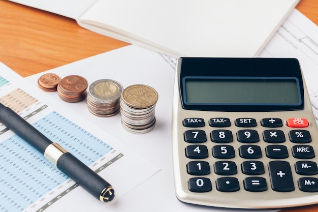 Pile of money coins with graph paper on wood table, concept in account, finance and growth of business 