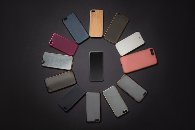 Куча разноцветных пластиковых задних крышек для мобильных телефонов на черном фоне с телефоном сбоку