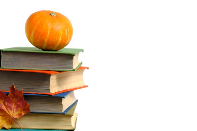 Pile old books pumpkin and autumn yellowed foliage white background