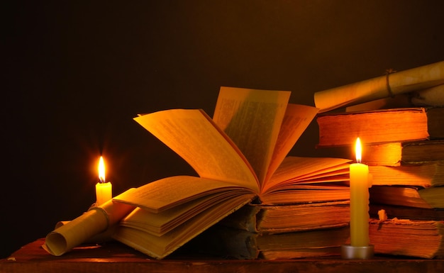 Pile of old books with candle and scroll in dark