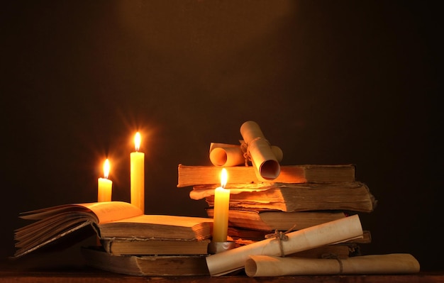 Pile of old books with candle and scroll in dark