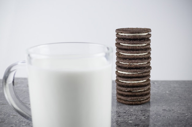 Pile of Oreo cookies and transparent cup of milk on gray granite table - Saint Petersburg, Russia, July 2021