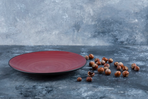 Pile of organic shelled hazelnuts with empty red plate.