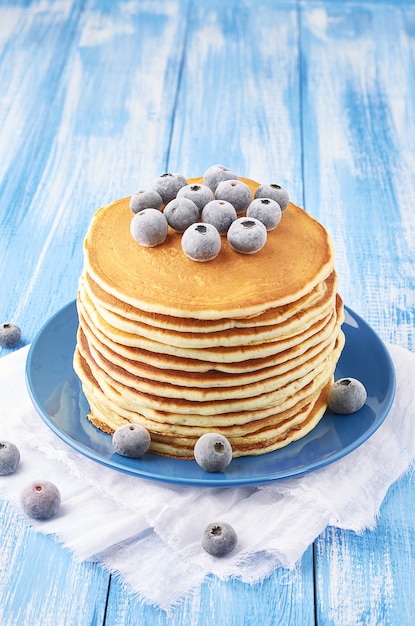 A pile of pancakes stuffed with frozen blueberry on a blue plate on a blue background sprinkled with powdered sugar