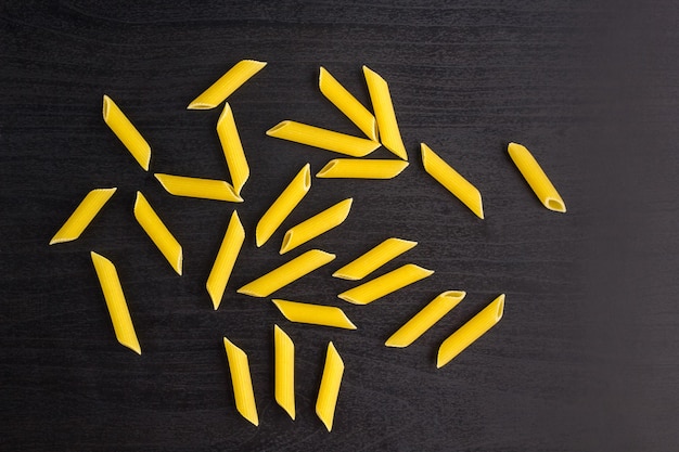 A pile of penne pasta on black background